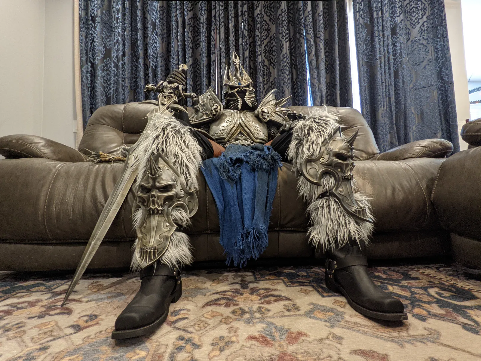 The Lich King armor by Hoku Props seated, fur greaves, tabard and sword across the lap