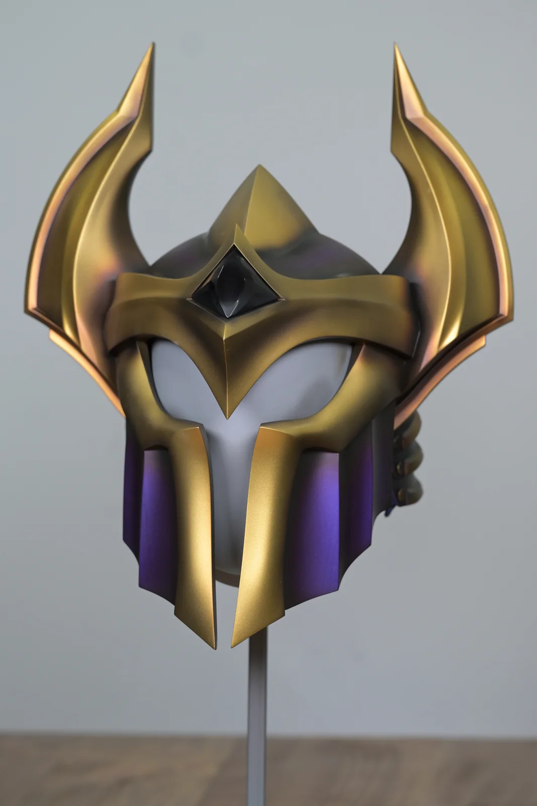 The Champions Queue helmet by Hoku Props on a display stand before assembly, brushed gold horns and color-shift purple faceplate