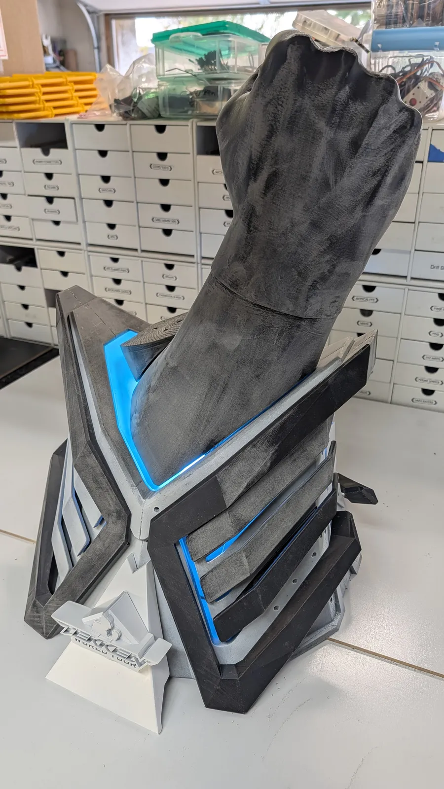 The TEKKEN World Tour 2025 trophy by Hoku Props in primer on the bench, crossed fists over a lit chevron base