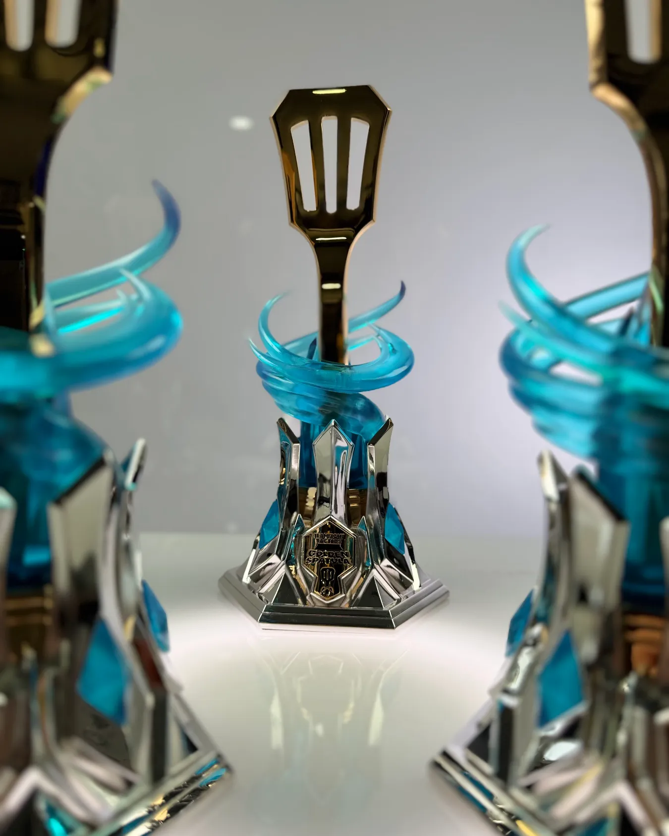 Two Golden Spatula trophies by Hoku Props on a white sweep, the front one sharp and the chromed base catching the light
