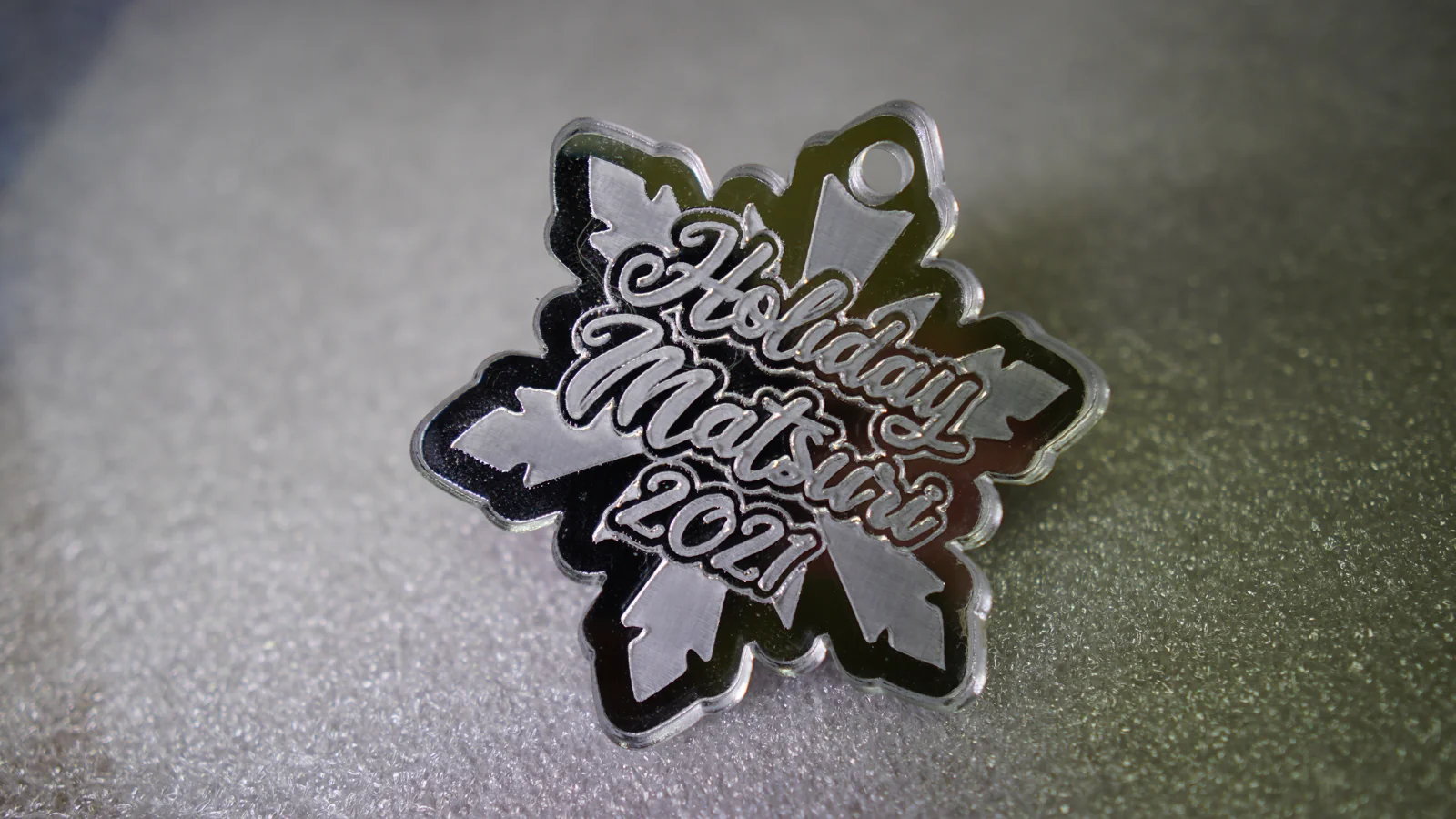 A laser-cut mirrored Holiday Matsuri 2021 snowflake ornament by Hoku Props