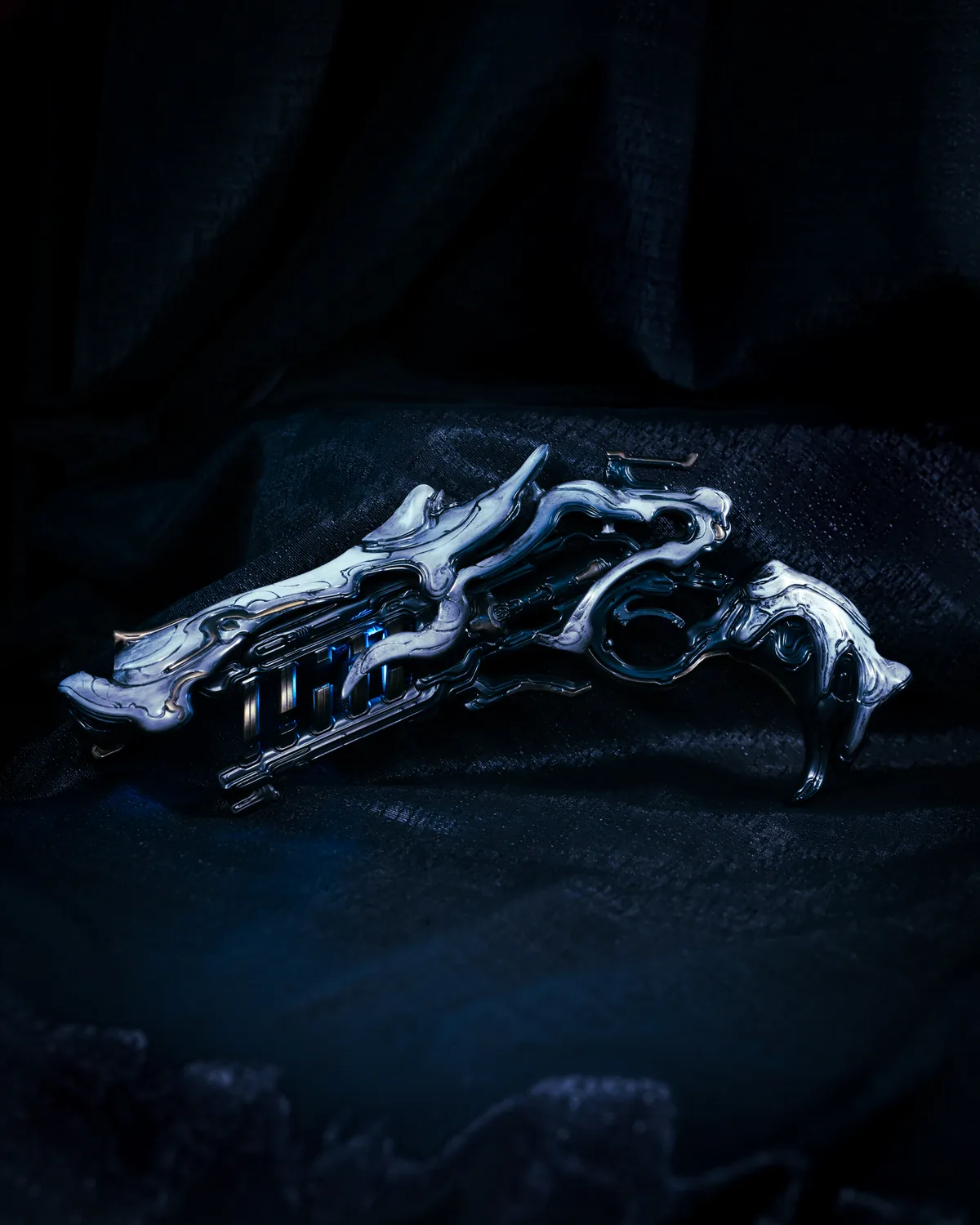 The Sirocco pistol prop by Hoku Props, a chrome organic sidearm with gold accents and a blue energy core, lit on dark fabric