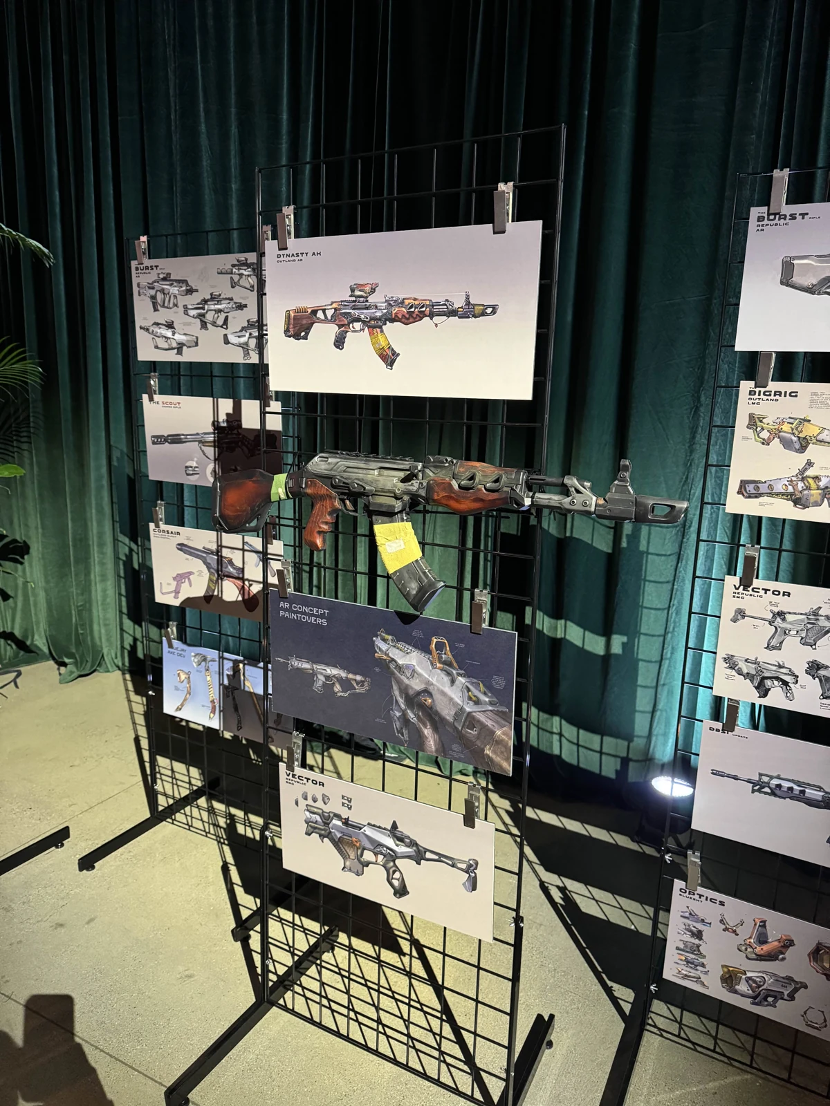 The Hoku Props Dynasty rifle replica displayed on a grid wall beside its Highguard concept art at a Wildlight Entertainment event