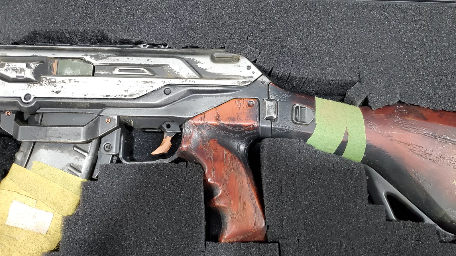Detail of the Highguard Dynasty rifle replica grip and stock, hand-painted wood grain and worn metal, in its foam case