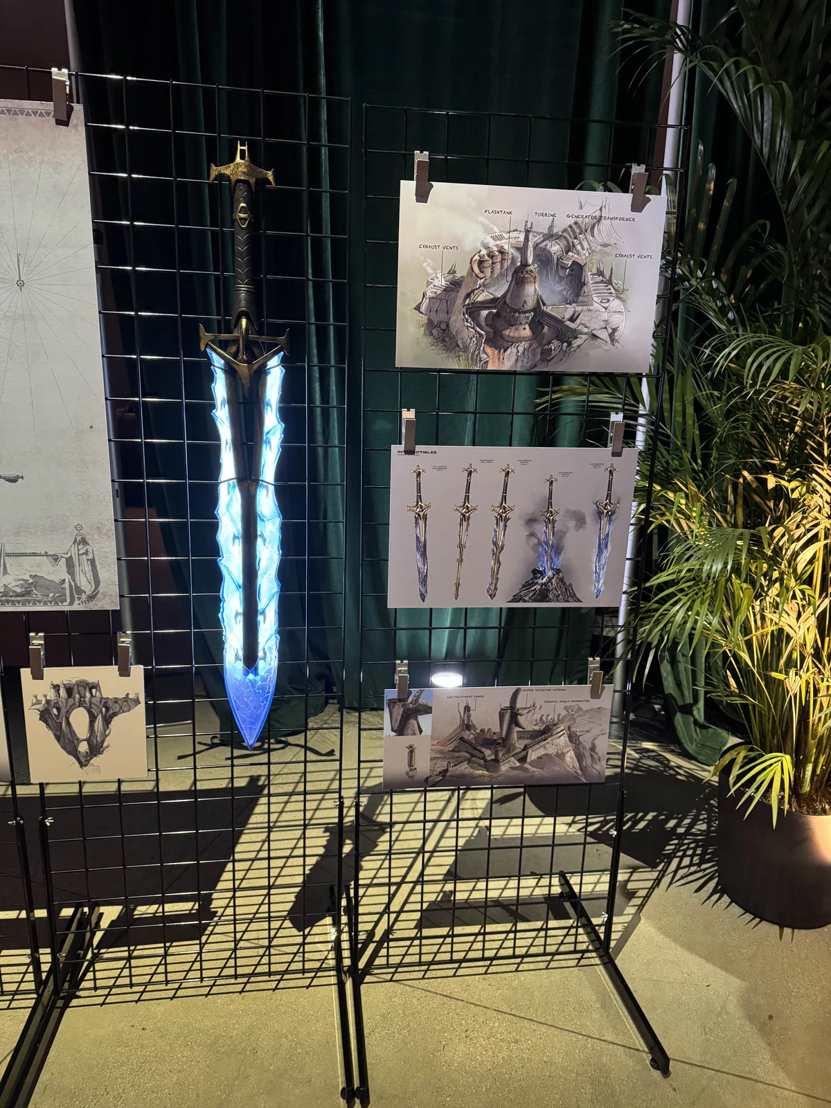 The Hoku Props Shieldbreaker sword replica with its blade lit, displayed next to Highguard concept art at a Wildlight Entertainment event