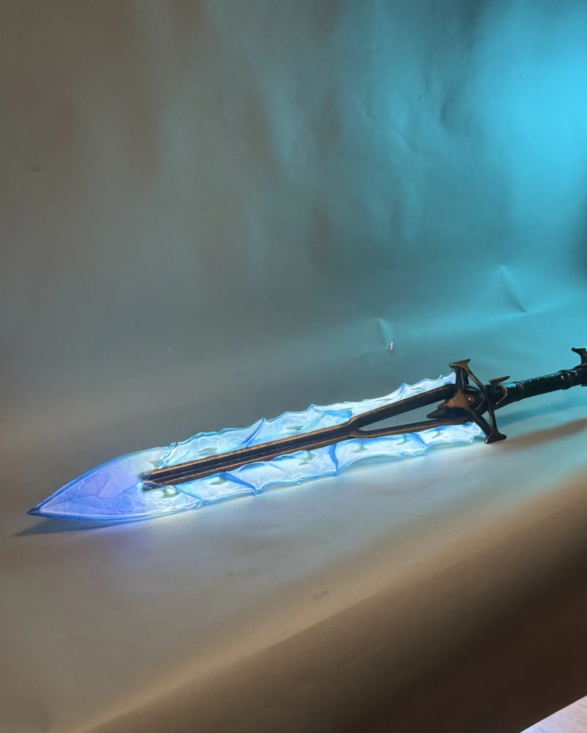 The Highguard Shieldbreaker sword replica by Hoku Props with an illuminated translucent blue blade, on a teal studio backdrop